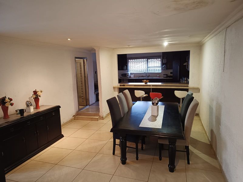 Open plan dining area featuring tiled floors and a breakfast bar overlooking the kitchen, with visible ceiling and wall maintenance required.