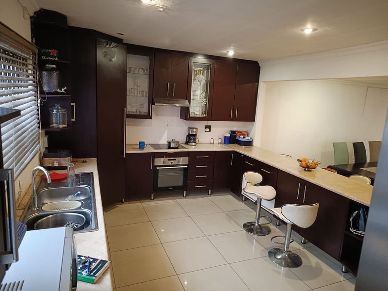 A functional kitchen featuring dark wood cabinetry, a breakfast bar, integrated oven and hob, and tiled flooring, offering a practical layout for daily use.