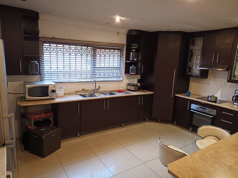 A functional kitchen featuring dark cabinetry, laminate countertops, and built-in appliances, requiring some cosmetic attention to the walls and ceiling.