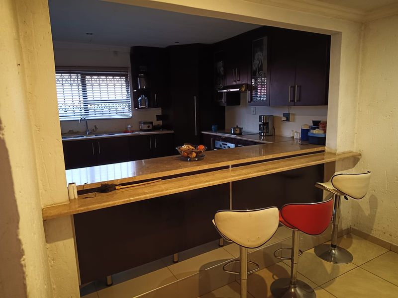 A functional kitchen featuring dark cabinetry, a stone breakfast bar, and integrated appliances, with an open-plan layout connecting to the adjacent living space.