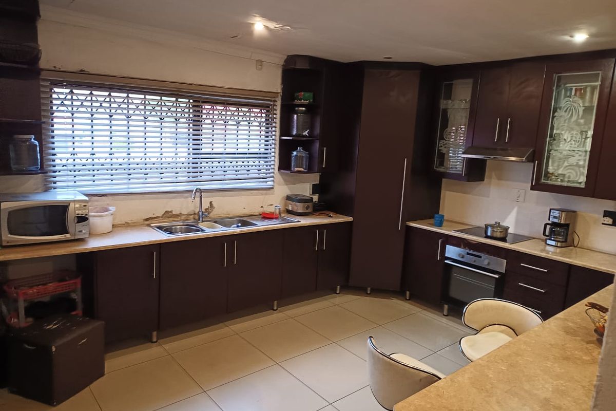 A functional kitchen featuring dark wood cabinetry, laminate countertops, and built-in appliances, requiring some cosmetic repairs to the wall and ceiling finishes.