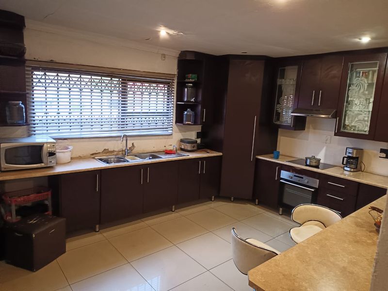 A functional kitchen featuring dark wood cabinetry, laminate countertops, and built-in appliances, requiring some cosmetic repairs to the wall and ceiling finishes.