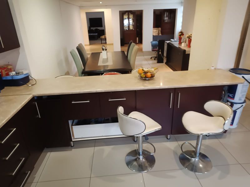 Open plan kitchen area featuring dark cabinetry, stone countertops, and tiled flooring, with a breakfast bar overlooking the dining space.
