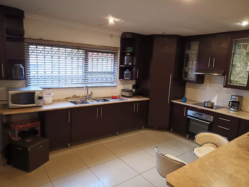 A dated kitchen featuring dark cabinetry, tiled flooring, and integrated appliances, currently showing signs of wear on the walls and ceiling.