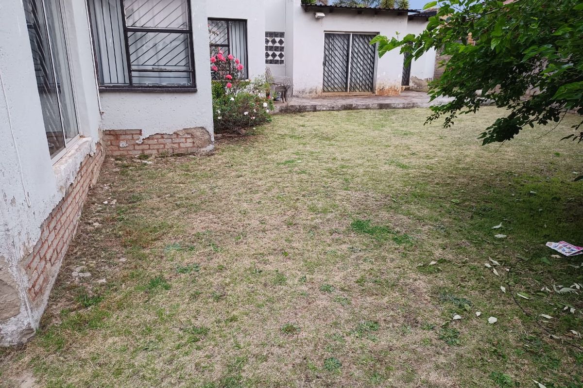 Rear garden area featuring a lawn, sliding doors with security gates, and visible wear to the exterior wall plaster and brickwork.