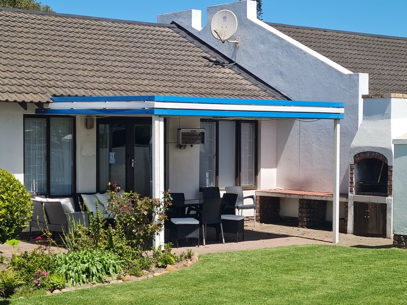 A covered patio area featuring a built-in braai, brick paving, and direct access to the garden through sliding doors.