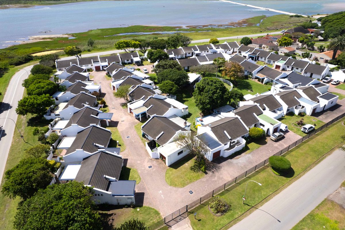 Aerial view of a residential townhouse complex featuring uniform architecture, paved driveways, and well-maintained communal gardens situated near a coastal lagoon.