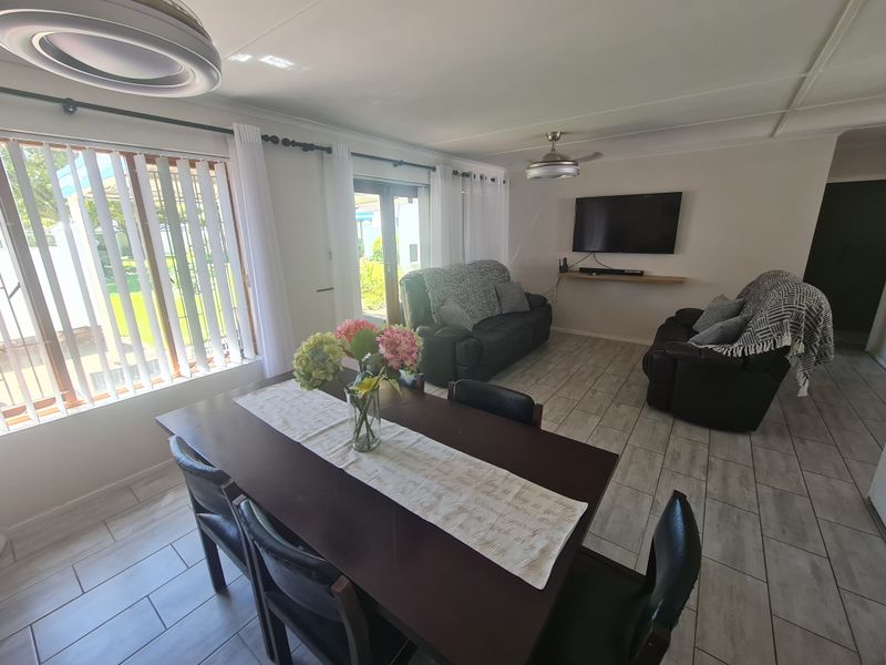 Spacious open-plan living and dining area featuring tiled flooring, a ceiling fan, and large sliding doors providing access to the garden.