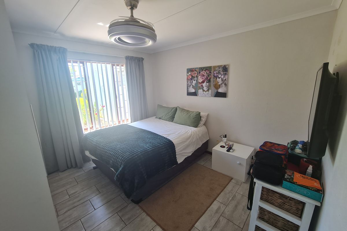 A functional bedroom featuring tiled flooring, a ceiling fan, and vertical blinds, providing a comfortable and practical living space.