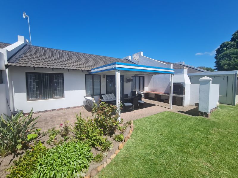 Rear exterior view of the townhouse featuring a paved patio with a covered pergola, built-in braai, and a well-maintained garden.