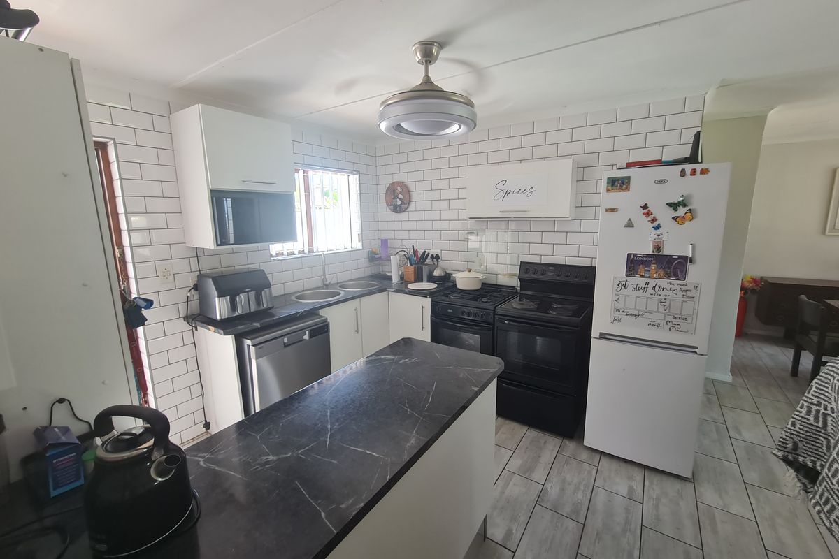 A functional kitchen featuring white subway tile backsplash, dark laminate countertops, built-in cabinetry, and a freestanding oven with an integrated extractor fan.