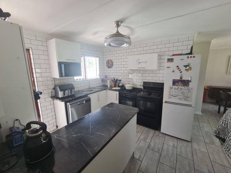 A functional kitchen featuring white subway tile backsplash, dark laminate countertops, built-in cabinetry, and a freestanding oven with an integrated extractor fan.