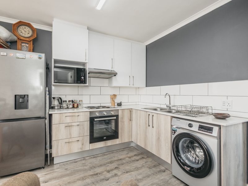 A modern kitchen featuring light wood-look cabinetry, white subway tile backsplash, built-in oven, hob, extractor fan, and integrated laundry appliance space.