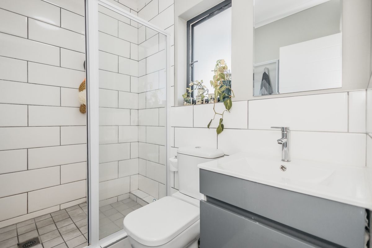 A modern, clean bathroom featuring a glass shower enclosure, subway wall tiling, a grey vanity cabinet with a basin, and a wall-mounted mirror.