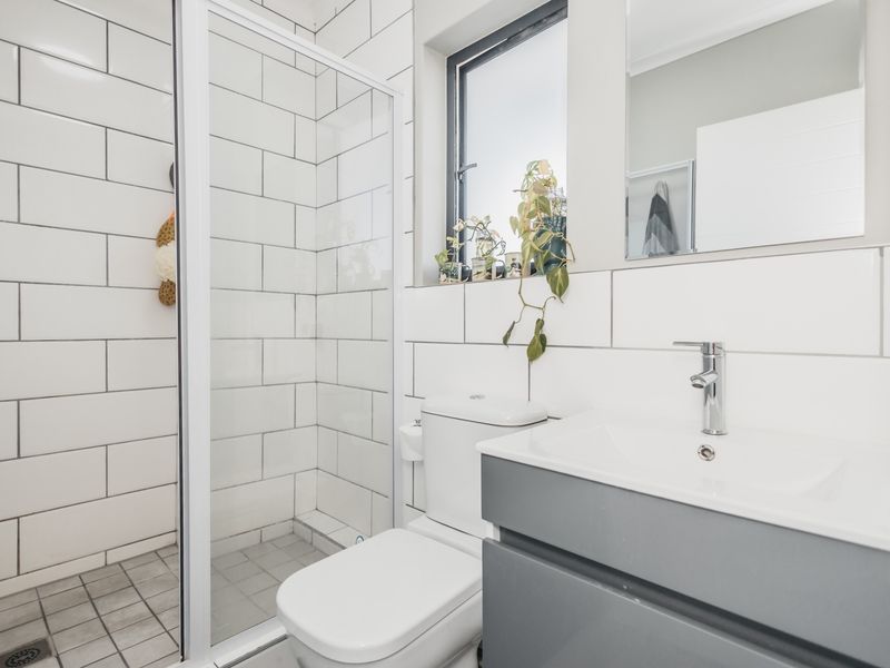 A modern, clean bathroom featuring a glass shower enclosure, subway wall tiling, a grey vanity cabinet with a basin, and a wall-mounted mirror.