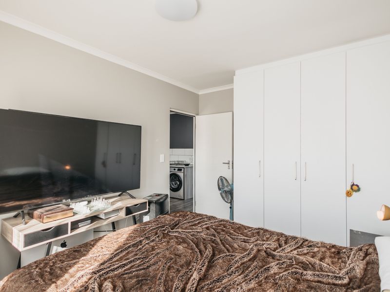 A well-maintained bedroom featuring ample built-in cupboard storage and neutral wall finishes, with a view into an adjacent laundry area.