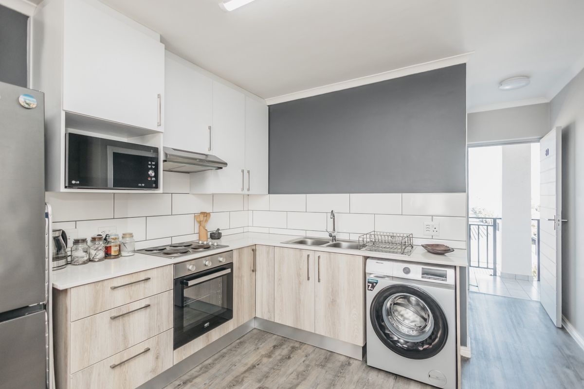 Modern kitchen featuring light wood-finish cabinetry, white countertops, subway tile backsplash, and integrated appliances including an oven, hob, and washing machine connection.