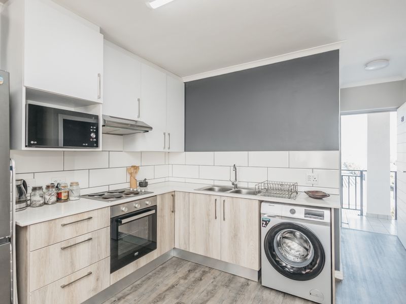 Modern kitchen featuring light wood-finish cabinetry, white countertops, subway tile backsplash, and integrated appliances including an oven, hob, and washing machine connection.