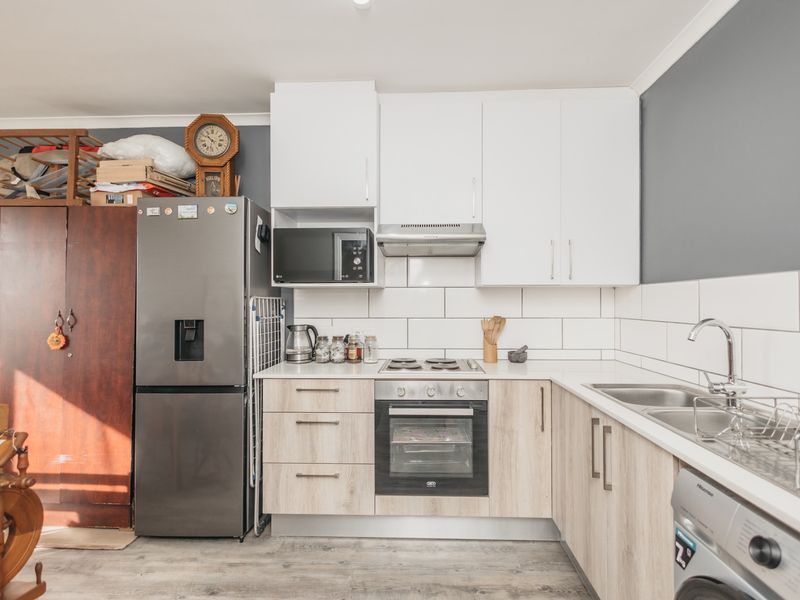 A functional kitchen featuring modern light wood cabinetry, white subway tile backsplash, integrated oven and hob, and a stainless steel sink.