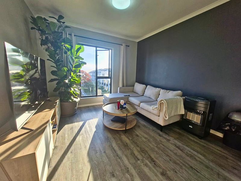 A well-lit living room featuring modern laminate flooring, a large window providing natural light, and a dark accent wall.
