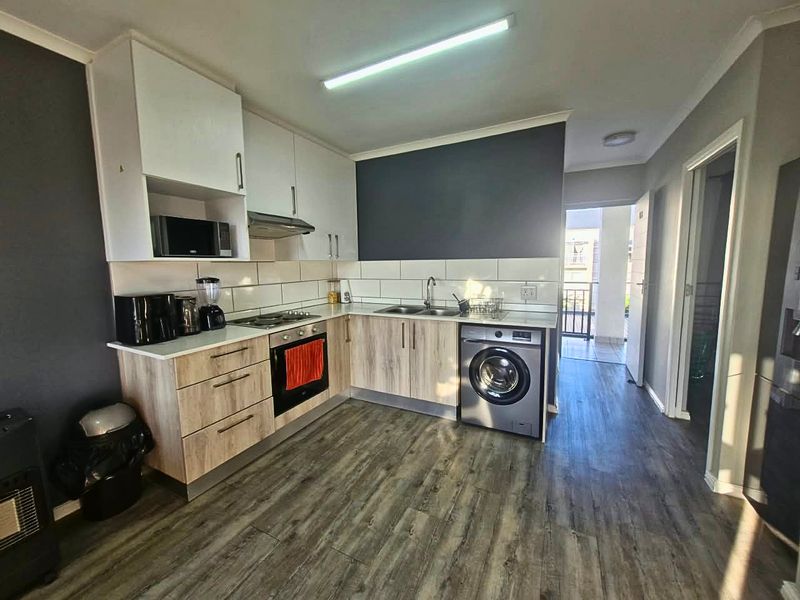 Modern kitchen featuring light wood-finish cabinetry, white upper cupboards, integrated appliances, and durable laminate flooring with direct access to an outdoor balcony area.