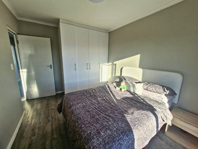 A well-maintained bedroom featuring laminate flooring, neutral wall tones, and a functional built-in wardrobe with clean white cabinetry.