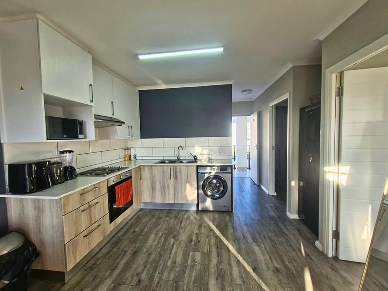 Modern kitchen featuring wood-look cabinetry, white upper cabinets, tiled backsplash, built-in oven, hob, and integrated washing machine with durable flooring.