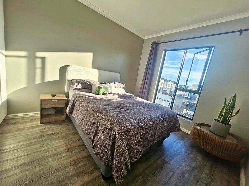 A well-lit bedroom featuring durable laminate flooring, a large casement window with natural light, and neutral wall finishes.