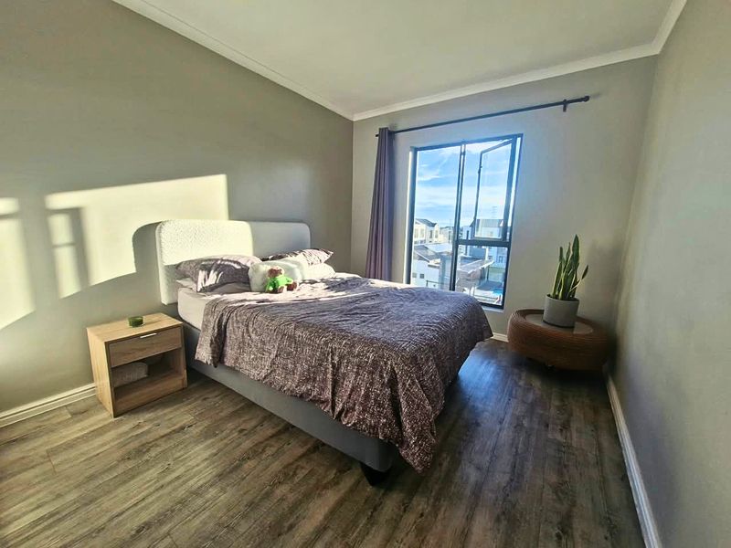A well-maintained bedroom featuring durable laminate flooring, neutral wall tones, and a large window that provides natural light and neighborhood views.