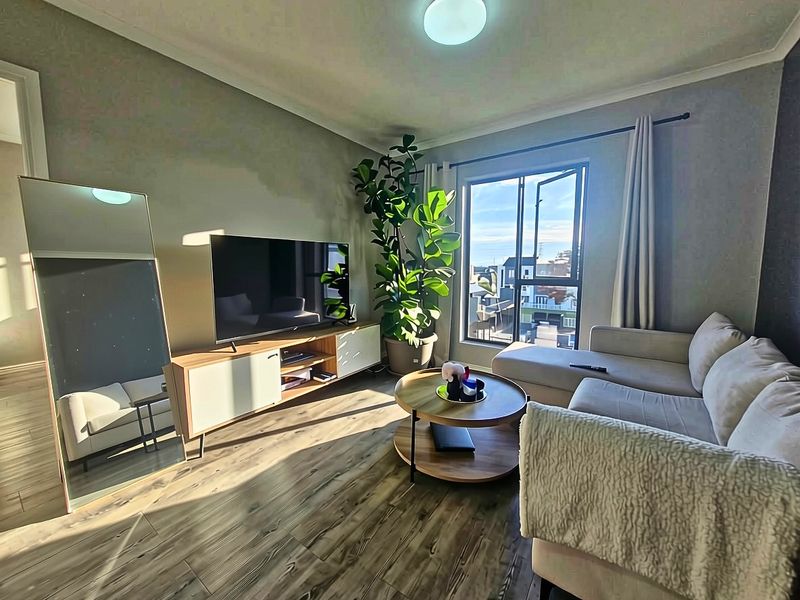A bright and comfortable living room featuring wood-look laminate flooring, large casement windows, and decorative cove cornicing.