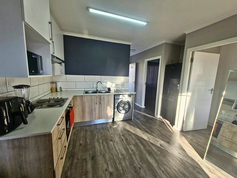 Modern kitchen featuring wood-look cabinetry, subway tile backsplash, integrated washing machine, and electric hob, with durable laminate flooring throughout.
