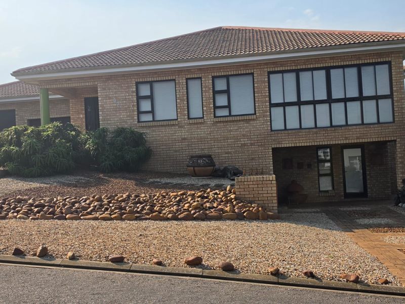 A well-maintained face brick house featuring a tiled roof, paved driveway, integrated garage, and a landscaped rock garden in the front yard.