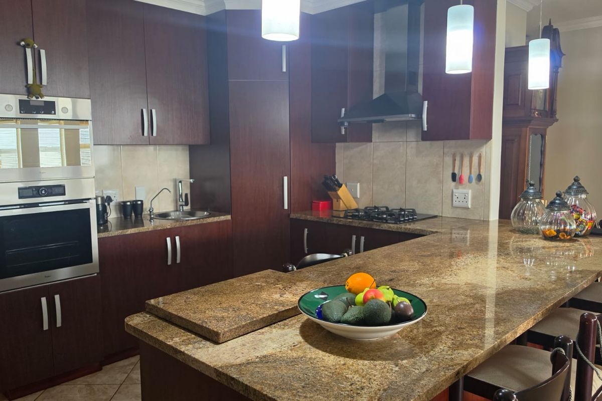 A well-appointed kitchen featuring dark wood cabinetry, granite countertops, a built-in oven and microwave, and a gas hob with an extractor fan.