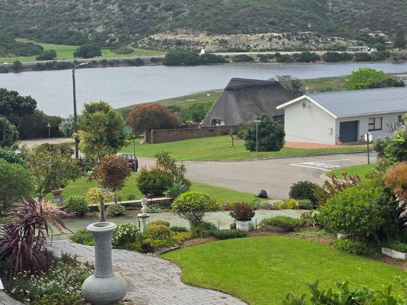 Elevated view overlooking a landscaped garden, paved pathways, and a scenic lagoon with surrounding hills.