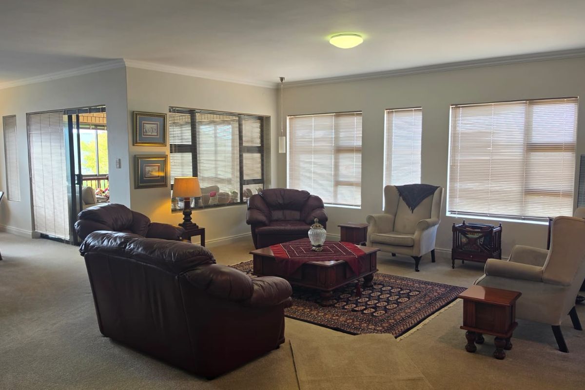 Spacious living room featuring neutral carpeting, large windows with venetian blinds, and access to an outdoor patio area through sliding glass doors.