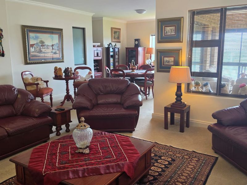 Spacious open-plan living and dining area featuring neutral carpeting, coved cornicing, and large windows with venetian blinds, offering a comfortable and functional layout.