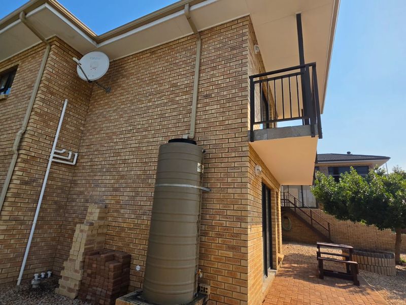 Rear exterior view of the brick house featuring a balcony, paved patio area, and a water tank installation.