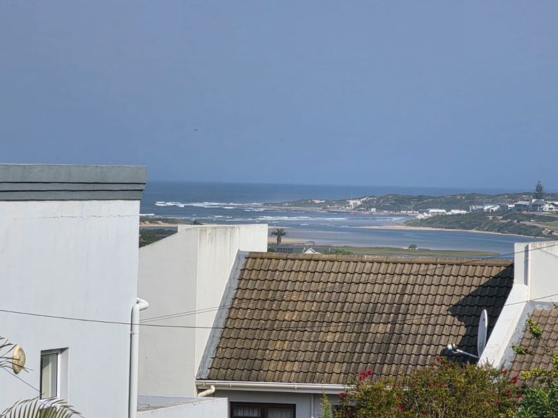 An elevated view overlooking the coastal landscape, estuary, and ocean, framed by the rooftops of neighboring properties.