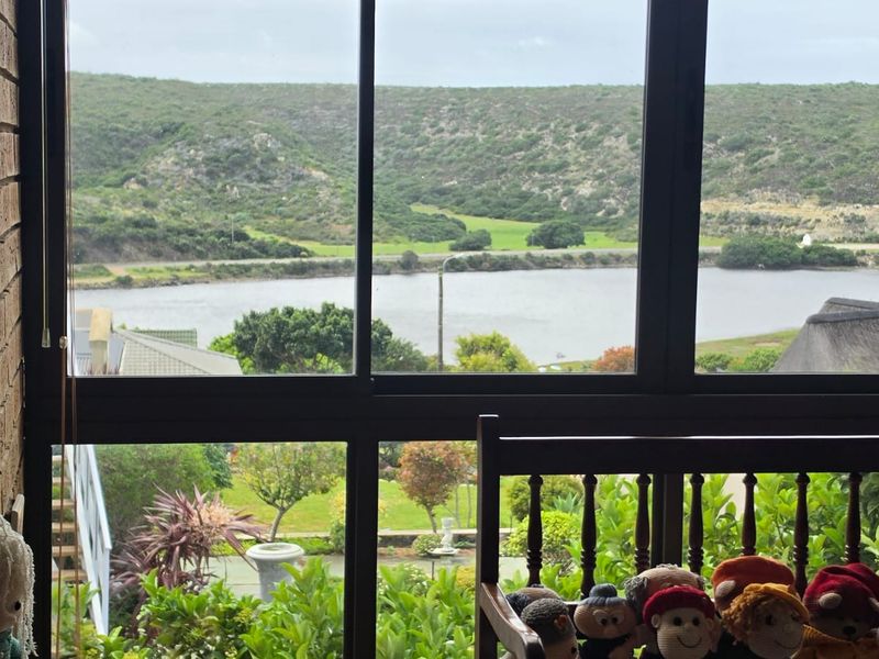 A view through a large window overlooking a river, green hills, and landscaped garden area.