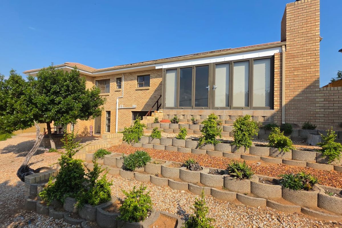 Rear view of the property featuring a brick facade, terraced retaining walls with established landscaping, and large glass sliding doors leading to the interior.