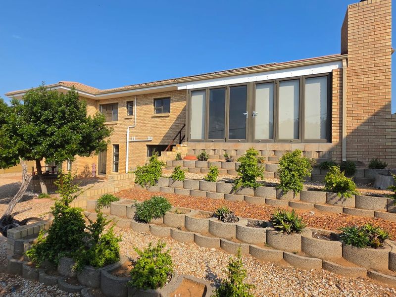 Rear view of the property featuring a brick facade, terraced retaining walls with established landscaping, and large glass sliding doors leading to the interior.
