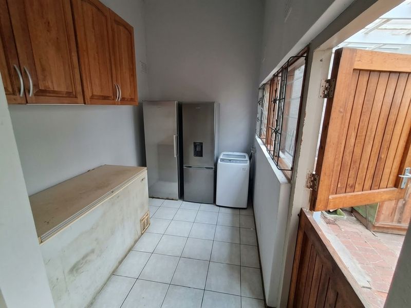 A functional laundry area featuring tiled flooring, wooden wall-mounted cabinetry, and a stable door leading to the exterior.
