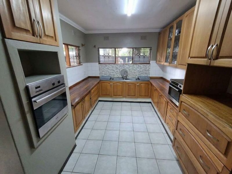 A functional kitchen featuring extensive wooden cabinetry, tiled flooring, a double sink, and built-in oven, offering a clean and practical workspace.