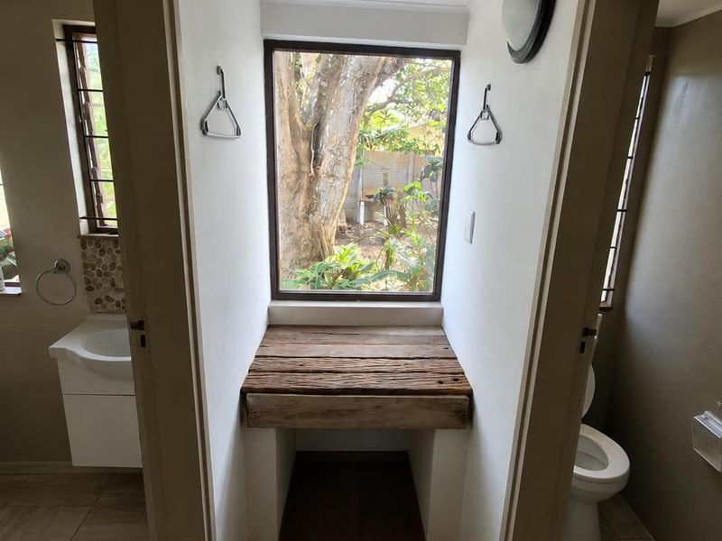 A small hallway area featuring a built-in wooden vanity shelf positioned beneath a window, flanked by access to a bathroom and toilet.