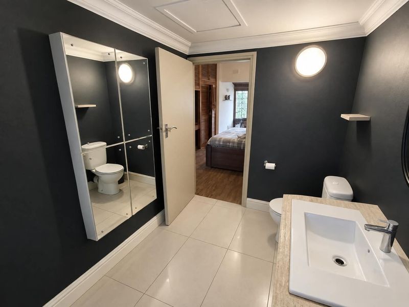 Modern bathroom featuring a vanity basin, toilet, tiled flooring, and dark accent walls with elegant crown molding.