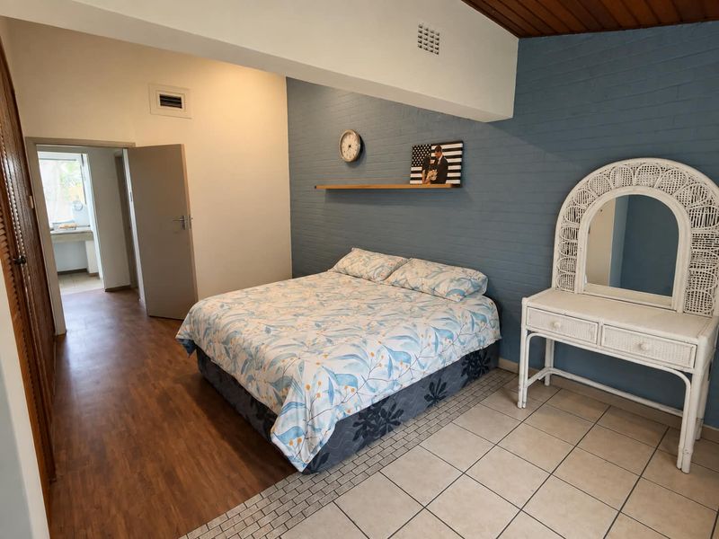 Spacious bedroom featuring a mix of laminate and tiled flooring, an exposed blue brick feature wall, and built-in cupboard storage.