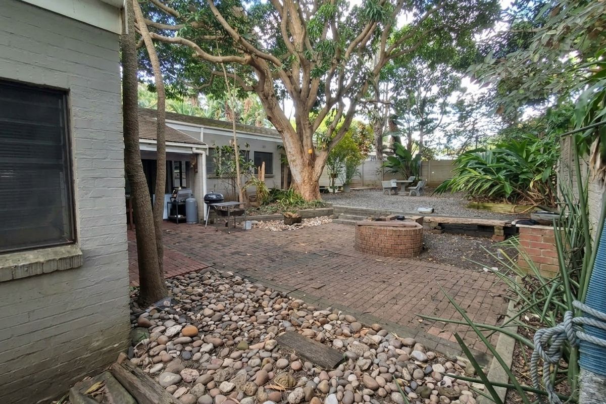 A private rear courtyard featuring brick paving, a built-in brick fire pit, and mature trees, offering a functional outdoor space for relaxation and entertaining.
