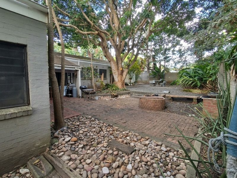 A private rear courtyard featuring brick paving, a built-in brick fire pit, and mature trees, offering a functional outdoor space for relaxation and entertaining.