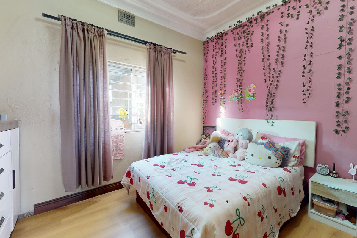 A bedroom featuring laminate flooring, ornate ceiling cornices, and a window fitted with security bars.