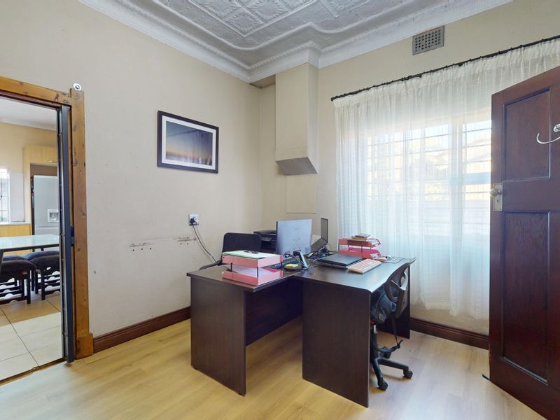 A functional home office space featuring laminate flooring and an ornate ceiling, with direct access to the adjacent kitchen area.